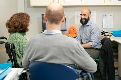 From left to right: trial participant Ailsa Guidi, sitting on a wheelchair. Next to her sits her partner Rob Guidi. On the right is trial physician Dr Sean Mangion, smiling. Image courtesy of the MS Society.