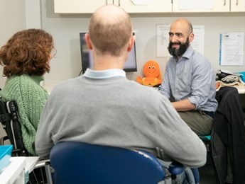 From left to right: trial participant Ailsa Guidi, sitting on a wheelchair. Next to her sits her partner Rob Guidi. On the right is trial physician Dr Sean Mangion, smiling. Image courtesy of the MS Society.