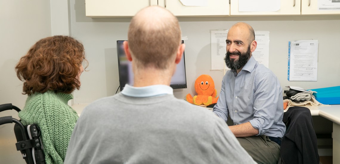 From left to right: trial participant Ailsa Guidi, sitting on a wheelchair. Next to her sits her partner Rob Guidi. On the right is trial physician Dr Sean Mangion, smiling. Image courtesy of the MS Society.