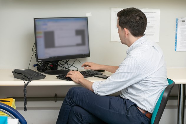 Dr Charles Wade (Octopus trial physician) facing away from the viewer typing at a computer in a medical office